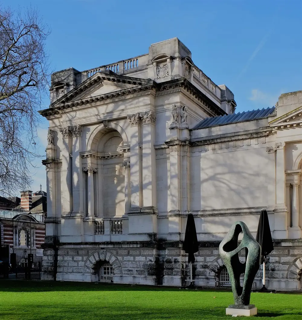 A stone corner pavilion of the Tate Britain building with a sculpture on the lawn